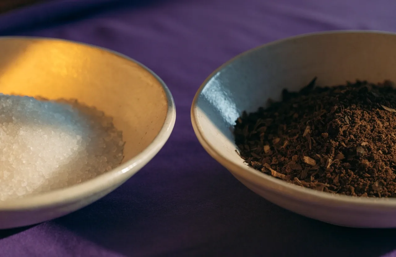 Zwei flache Keramikschalen mit Mineralsalz und gemahlenem Pflanzengut auf violettem Tuch